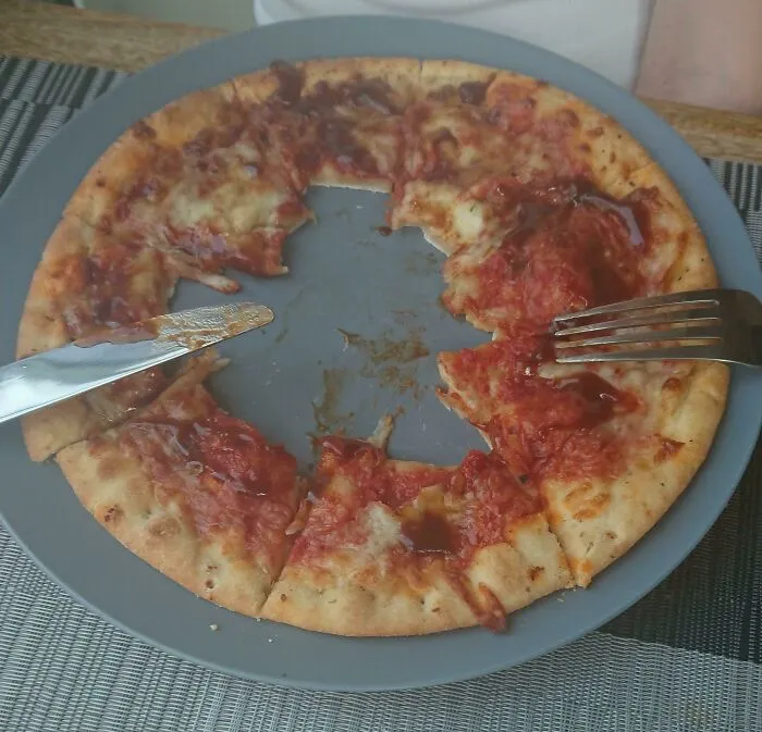 A pizza on a plate eaten only from the middle, showing a highly questionable decision