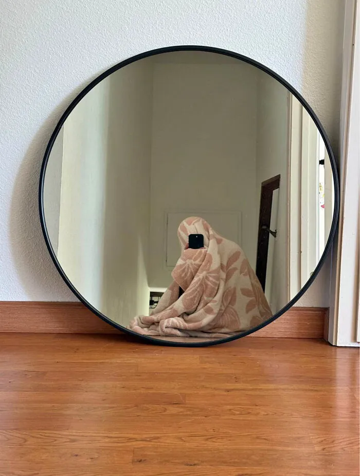 Funny mirror pic of a person completely covered in a patterned blanket taking a selfie in a large round mirror.