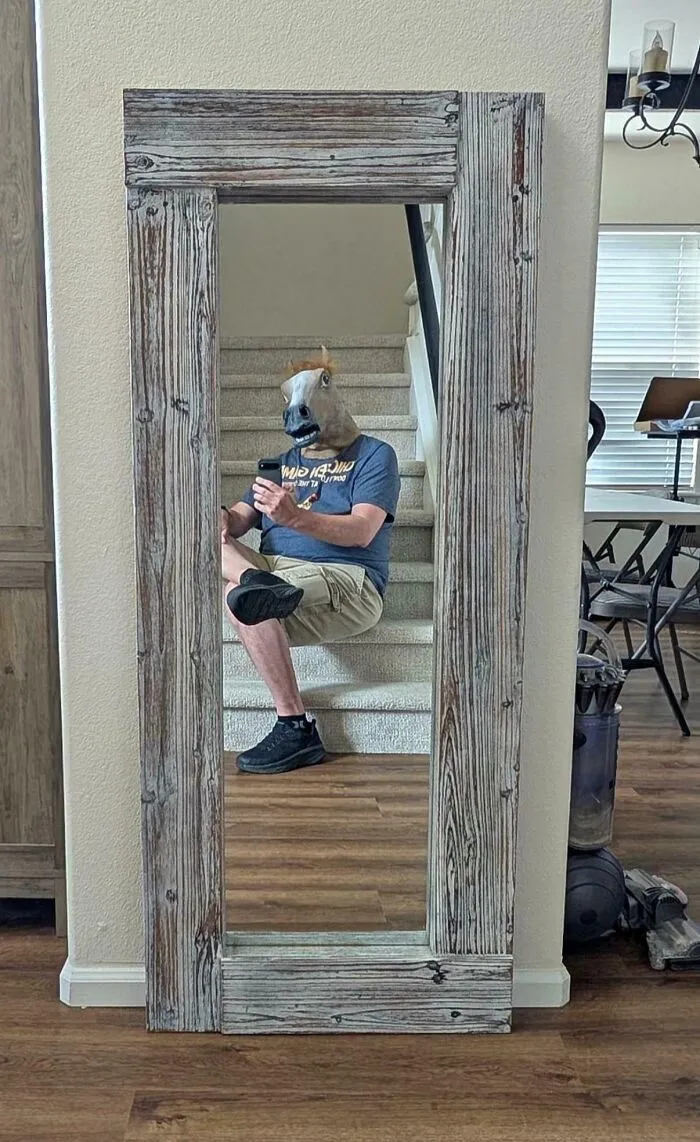 Funny mirror pic reflection of a person wearing a horse head mask sitting on the stairs
