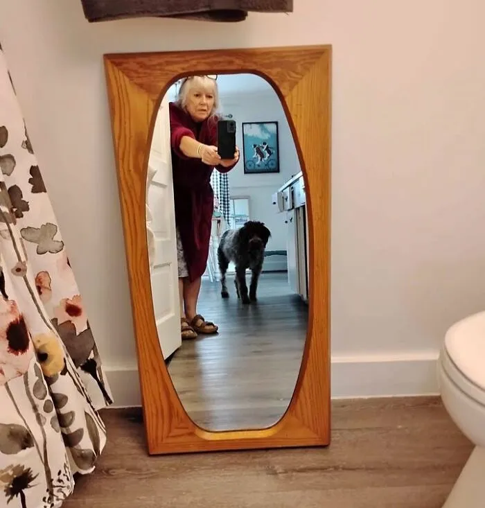 A funny mirror pic reflection showing a dog walking in the hallway while a person takes a photo