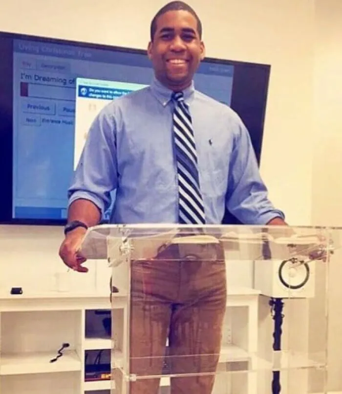 A man standing at a clear podium creating a funny reflection that looks like stained pants.