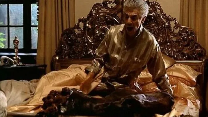 Man screaming in bed next to a prosthetic horse head, classic movie props.