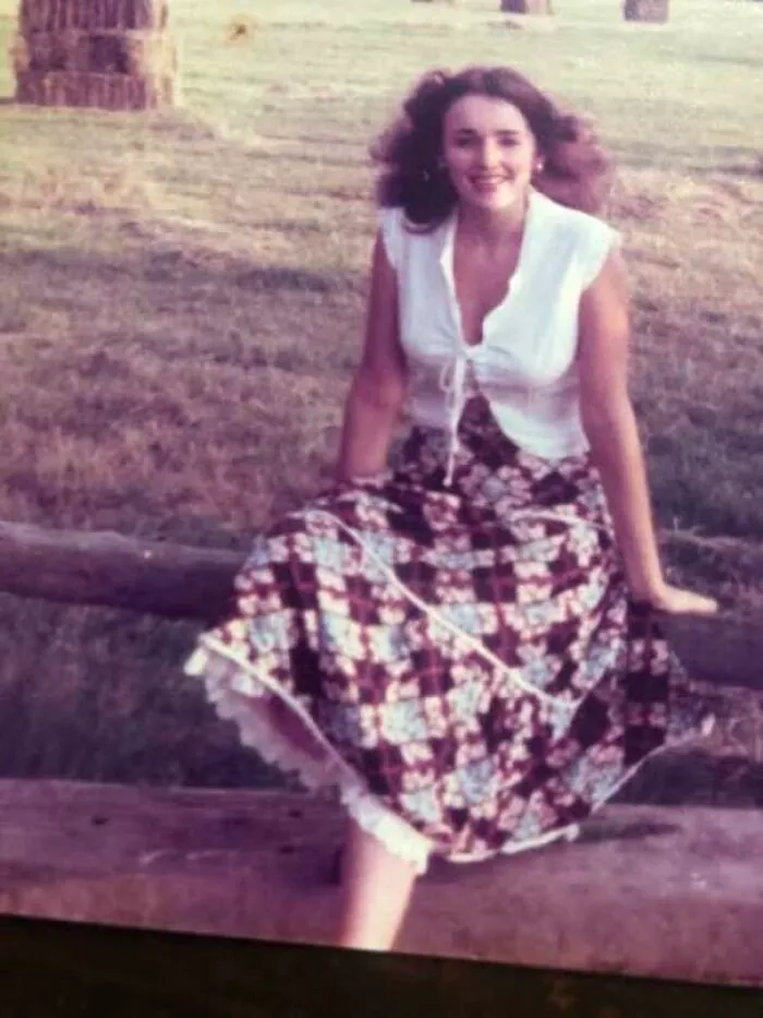 1970s outdoor portrait of woman sitting on fence wearing a floral maxi skirt