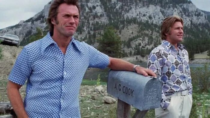 Clint Eastwood leaning on a mailbox in patterned shirts in retro '70s photos from a film set.