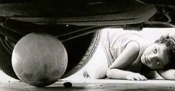 A young child reaching for a soccer ball under a car in vintage black and white 70s photos.