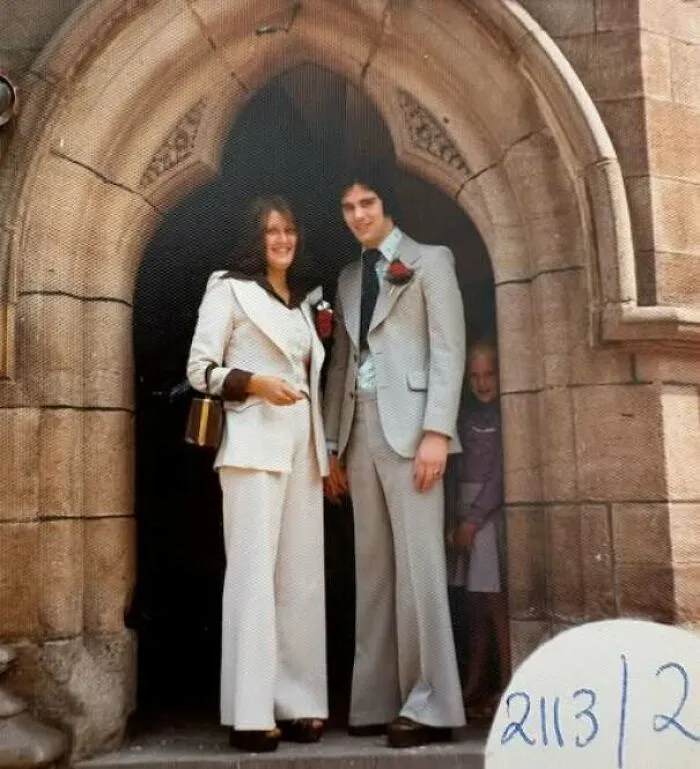 Vintage 70s photo of couple in retro wedding attire standing under stone arch