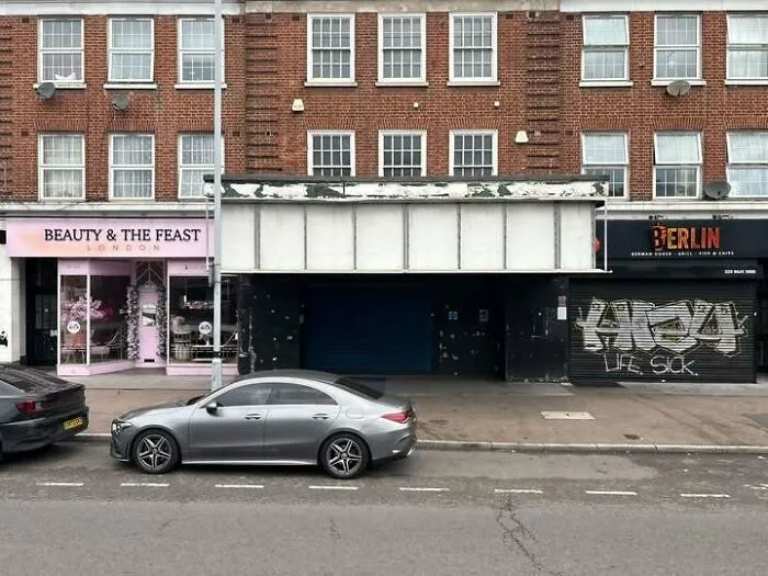 Empty 70s London street with worn storefronts and parked cars