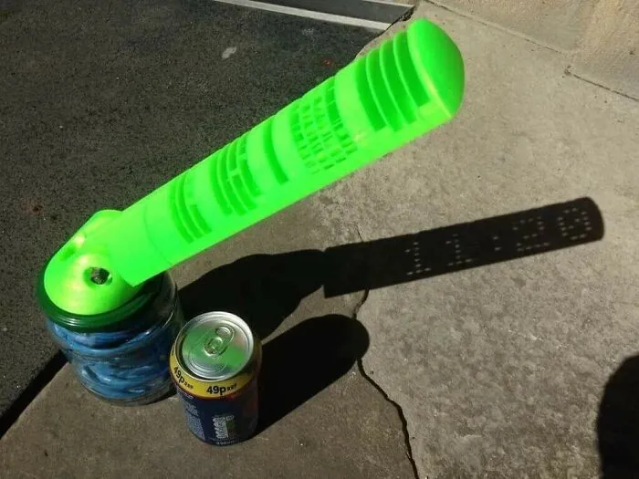 A lime green sundial made by a 3D printer casting a digital time shadow of 11:29 on the concrete