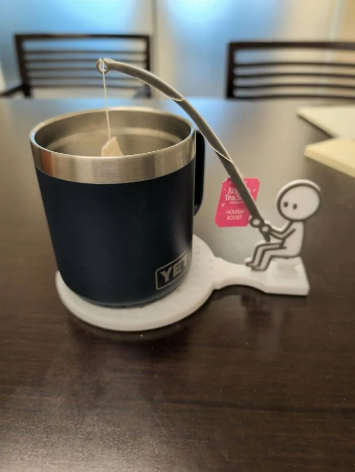 A creative 3D printer coaster shaped like a little person fishing a tea bag out of a mug.