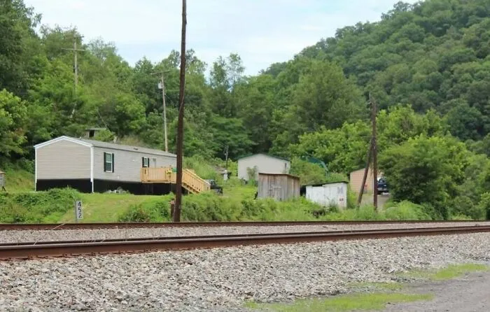 Rural homes near railway track surrounded by green hills and forest