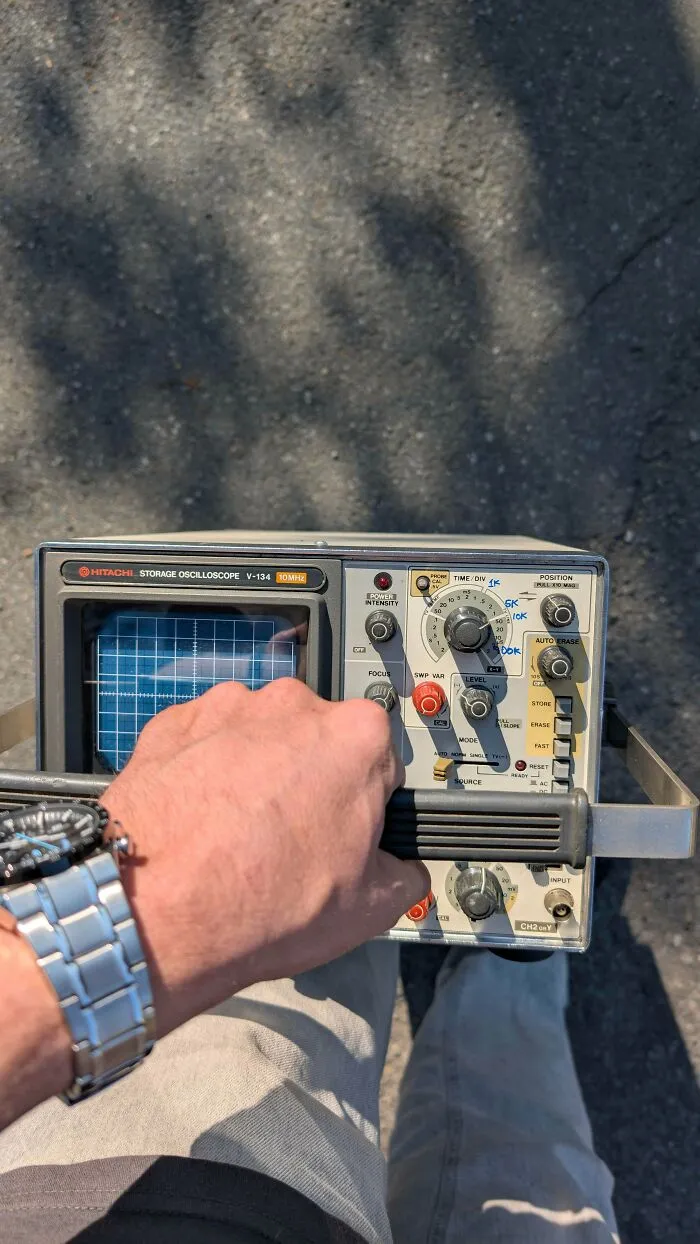 A hand holding a portable Hitachi storage oscilloscope, demonstrating classic retro gadgets and old electronics.