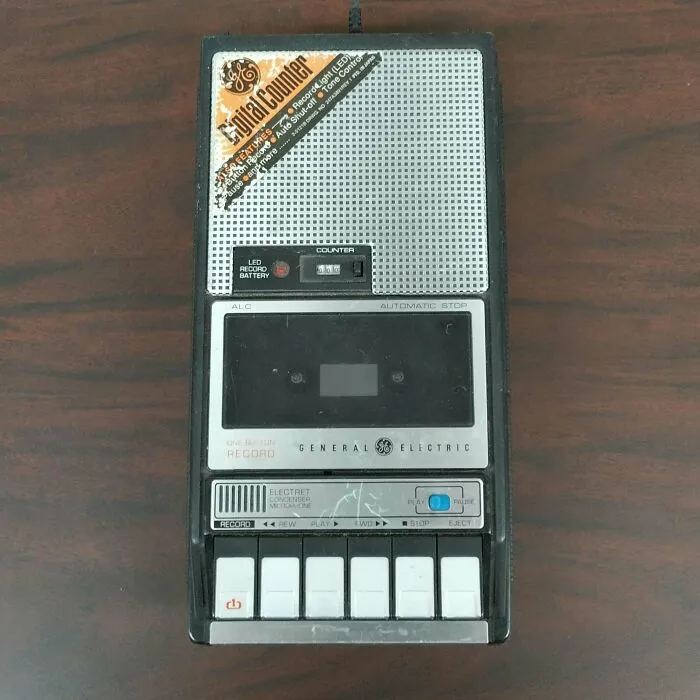 A vintage General Electric cassette tape recorder resting on a wooden surface, showing retro gadgets.