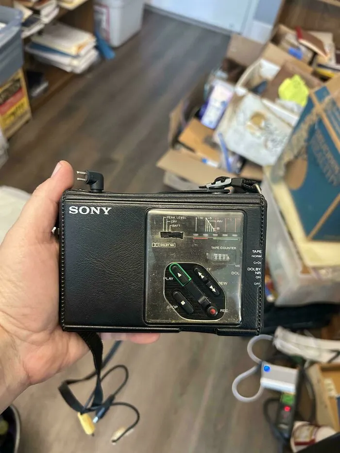 A hand holding a black leather-encased portable Sony tape recorder, demonstrating retro gadgets tech design.