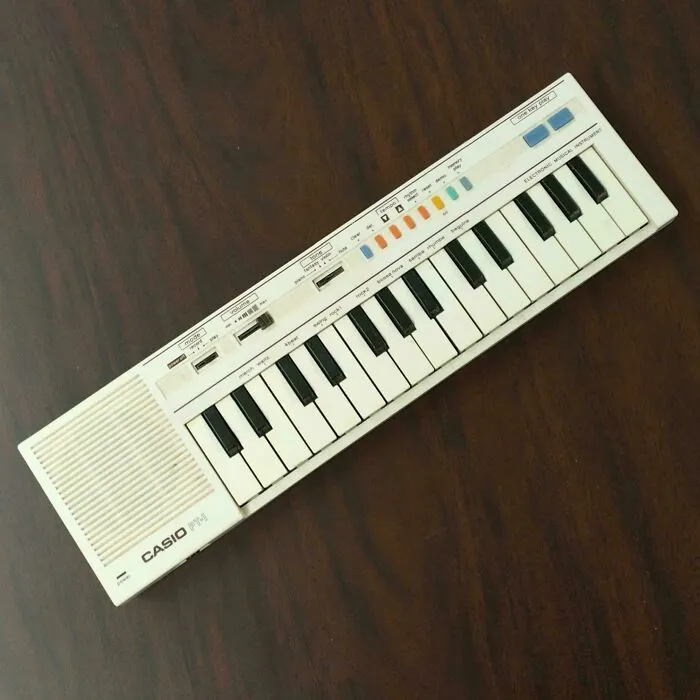 A white vintage Casio PT-1 electronic keyboard synthesizer resting on a dark wooden surface, showcasing retro gadgets.