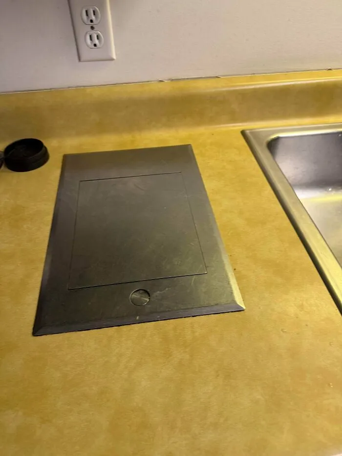 Vintage built in countertop appliance lid next to a kitchen sink, showcasing unique retro gadgets.