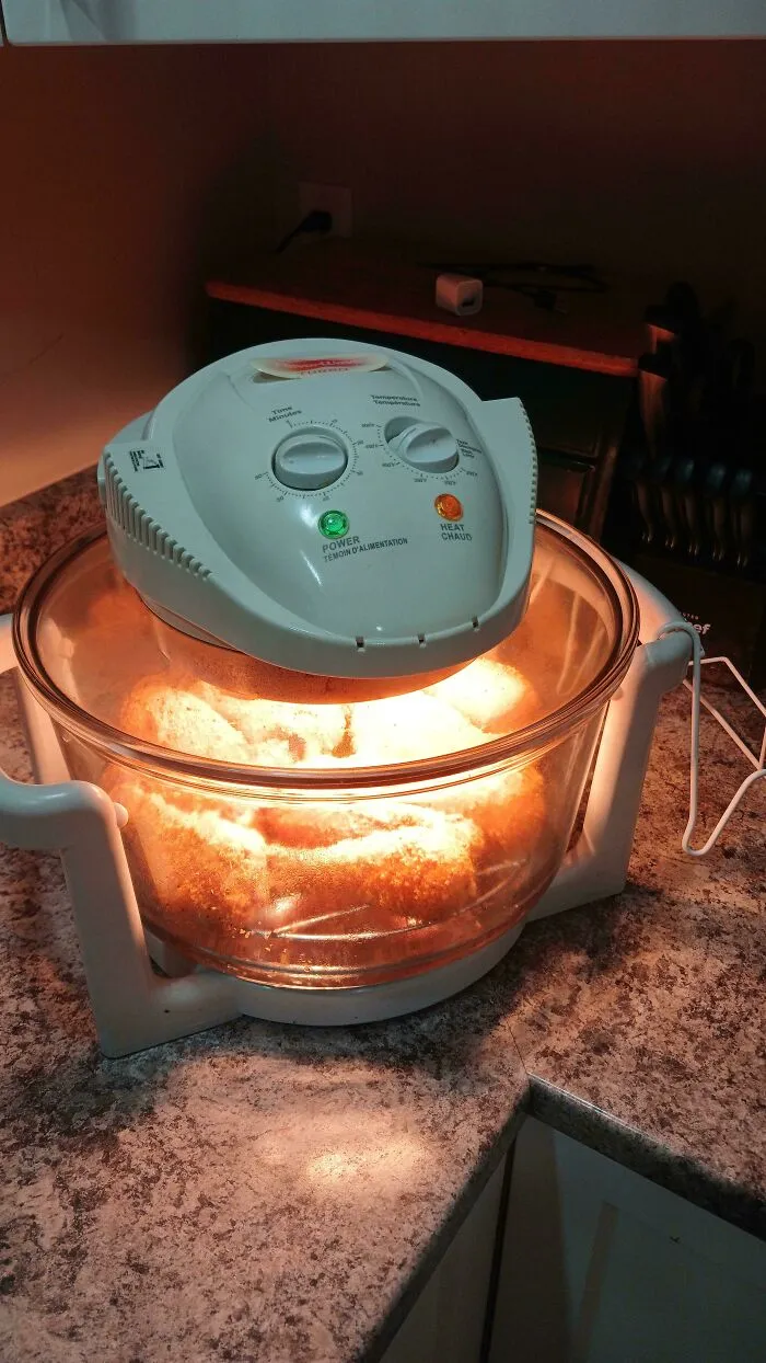A vintage round glass tabletop convection oven illuminating cooking food, an example of retro gadgets.