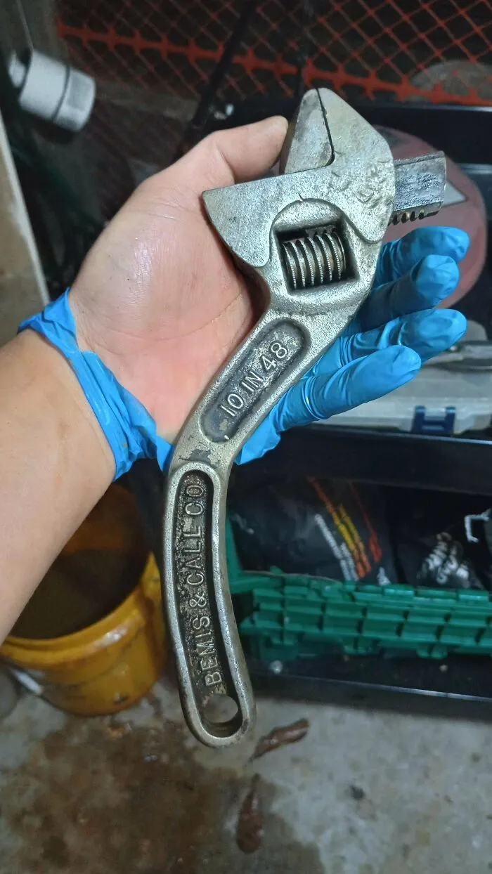 Hand wearing a blue glove holding a vintage Bemis and Call curved handle wrench as retro gadgets