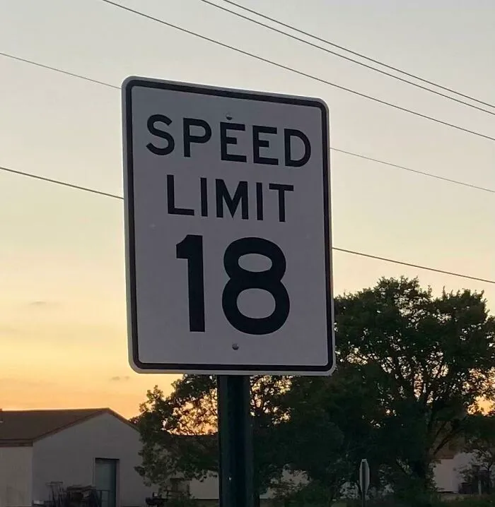 A strange road sign showing an unusual speed limit of 18 mph outdoors.
