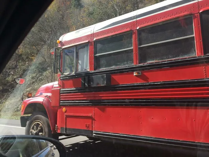 Strange photos of a red school bus driving along a road next to hills.