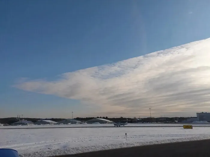 A strange photo capturing a perfectly straight line edge in the clouds over a snowy airfield.