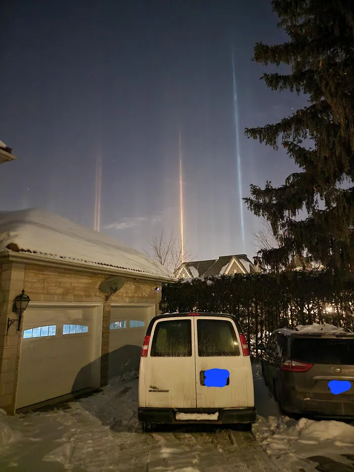 Light pillars streaming into the sky above parked cars, like strange photos from a surreal reality update.
