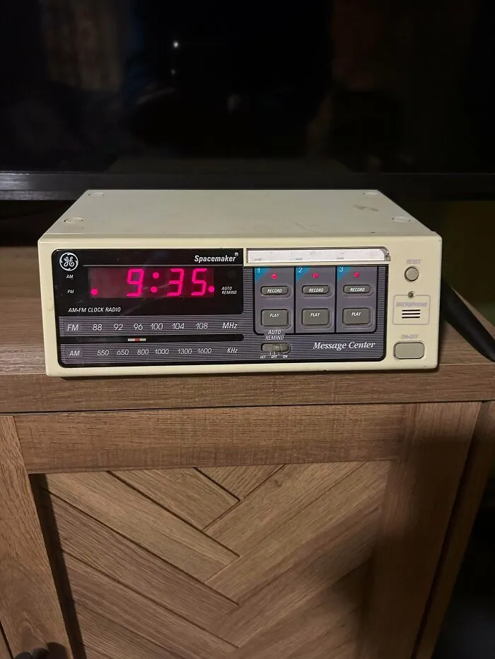 A retro GE Spacemaker clock radio and message center showing red digital time displays on a wooden cabinet.