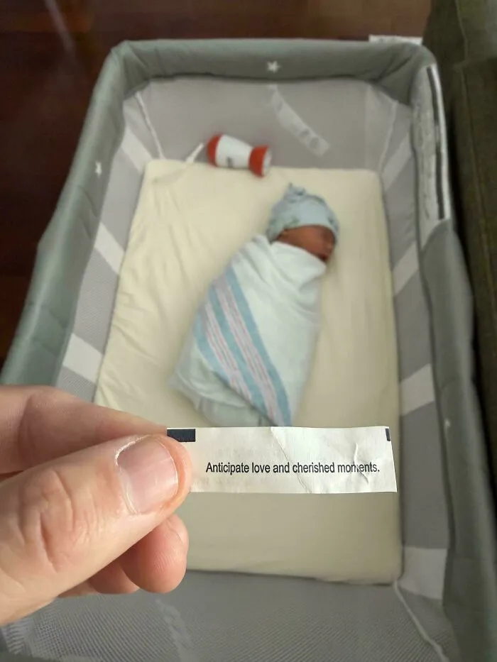A sleeping newborn baby in a bassinet next to a fortune cookie paper, representing wholesome dads moments.
