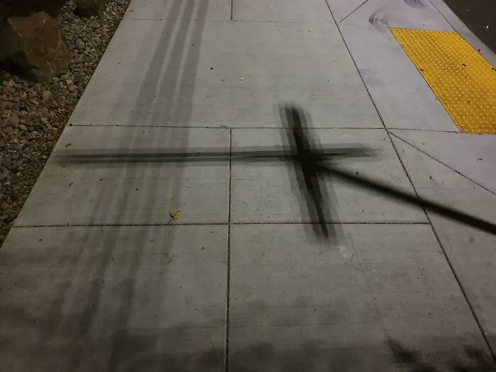 Cross-shaped shadow cast on a concrete sidewalk, capturing a strange photos moment.
