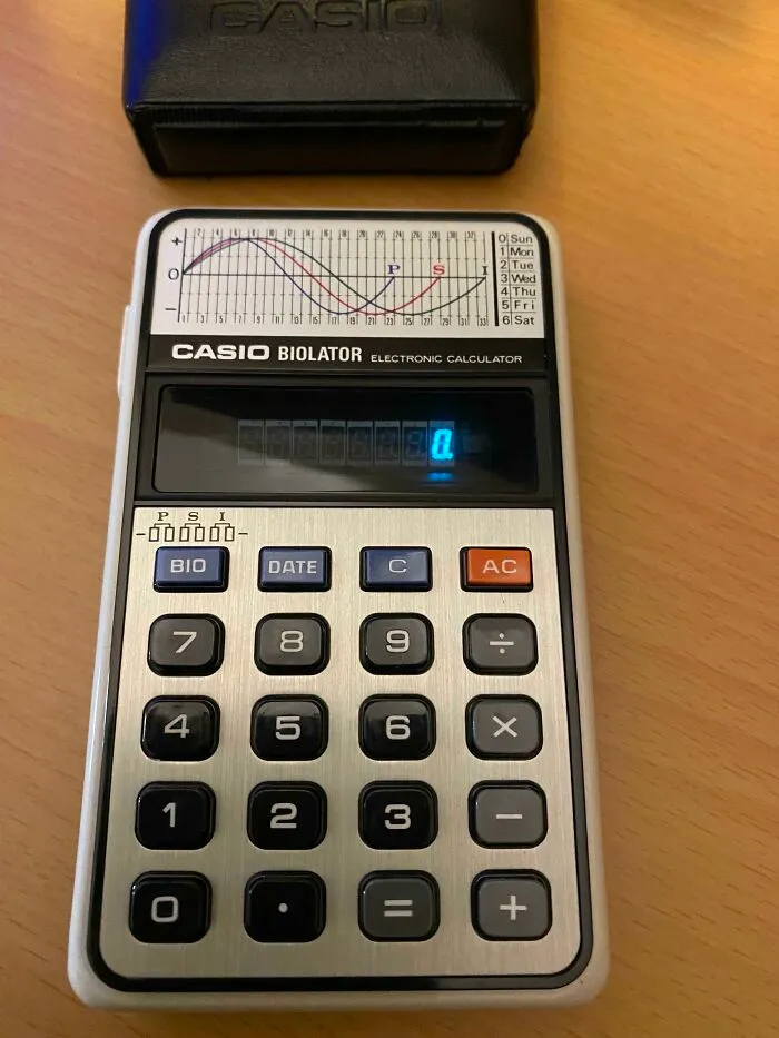 A retro Casio Biolator electronic calculator displaying a blue digital readout on a wooden surface.
