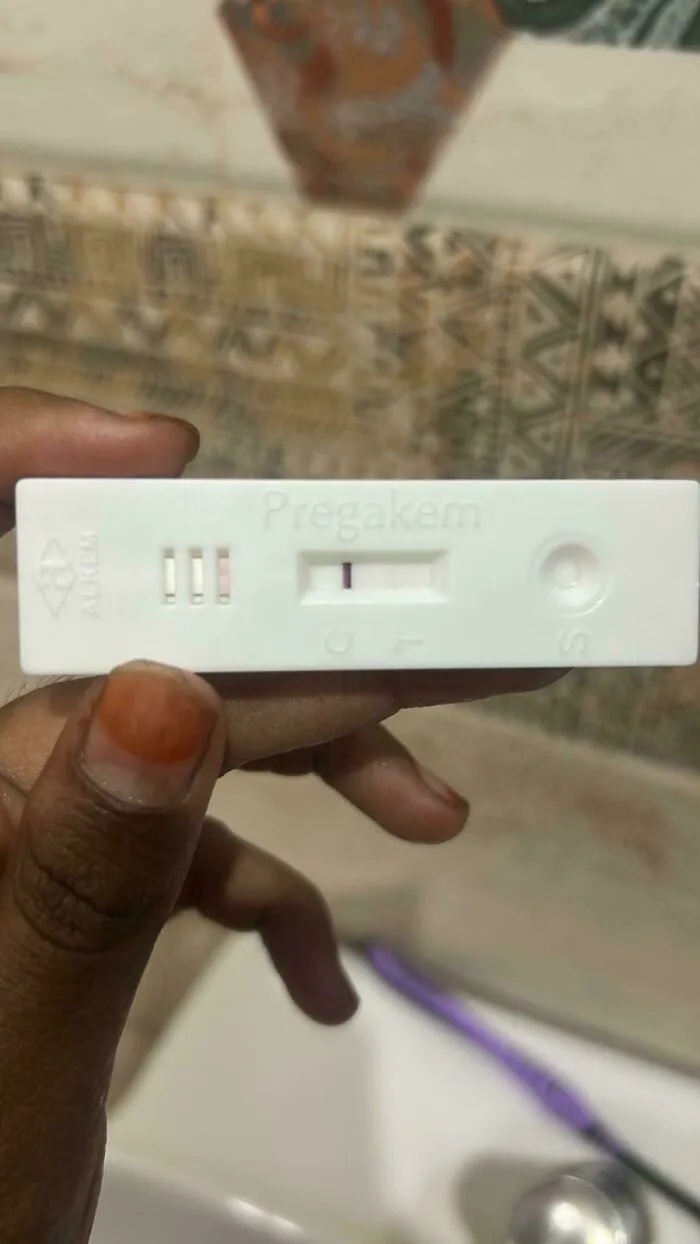 A hand holding a positive pregnancy test strip, representing wholesome pics of dads starting their fatherhood journey.