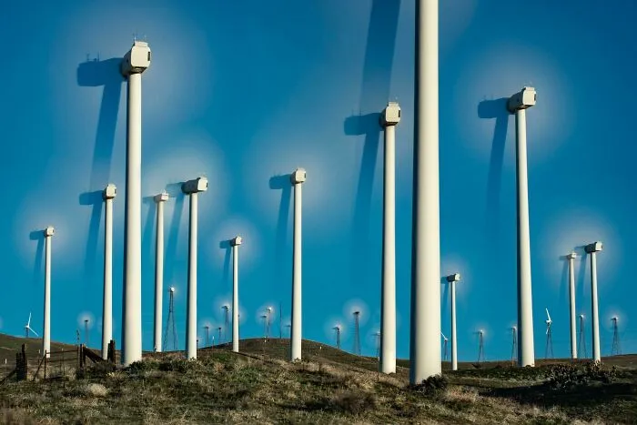 A field of tall wind turbines on a hill under a bright blue sky, featured in strange photos.