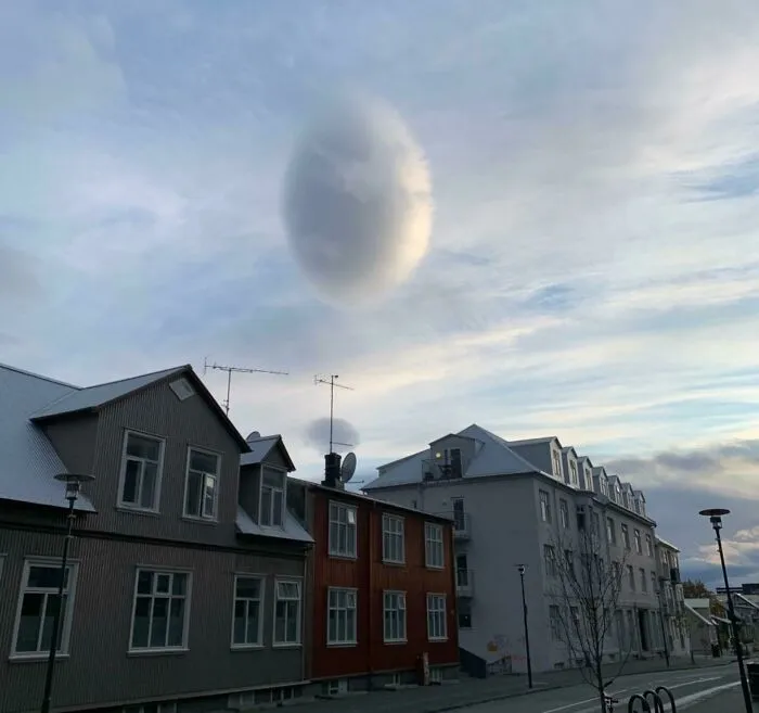 Strange photos of an oval lenticular cloud floating over residential houses like a glitched object.