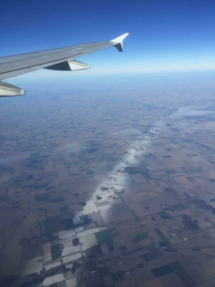 Strange photos view of airplane wing over fields with a line of mist appearing like a reality software glitch