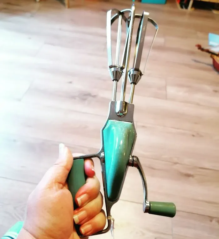A vintage hand-cranked egg beater with teal handles highlighting functional design in retro gadgets.