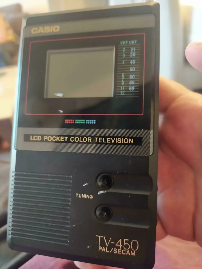 A black Casio LCD pocket color television held in a hand, showcasing retro gadgets.
