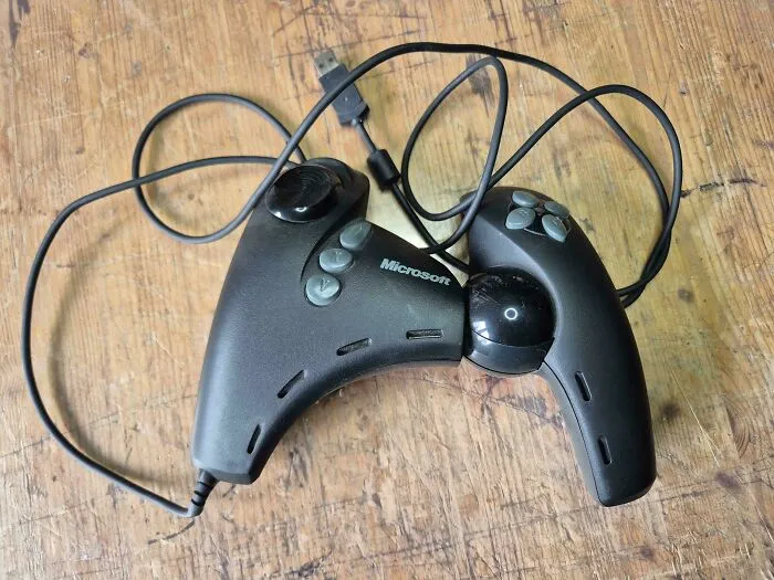 A black Microsoft SideWinder Dual Strike controller showcasing retro gadgets tech design on a wooden surface.