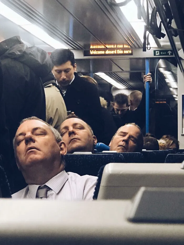Three men sleeping in a row on a train looking like identical clones in a strange photo.