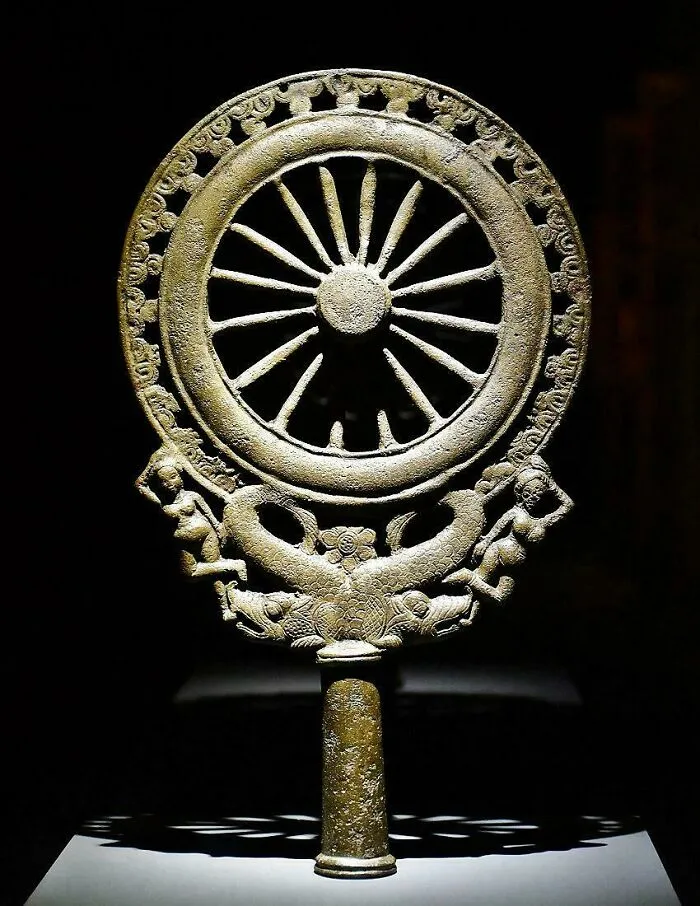 Ancient bronze artifact featuring a wheel and human figures