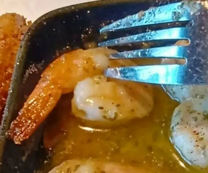 Shrimp in butter looking like a face staring with a fork.