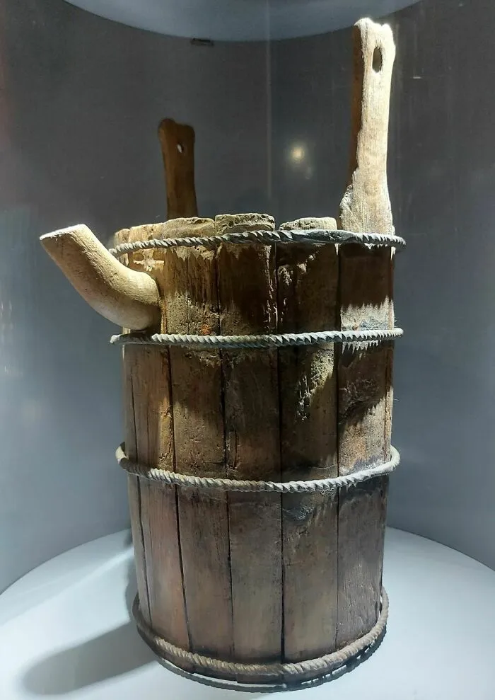 Ancient wooden bucket with spout and rope bindings on display