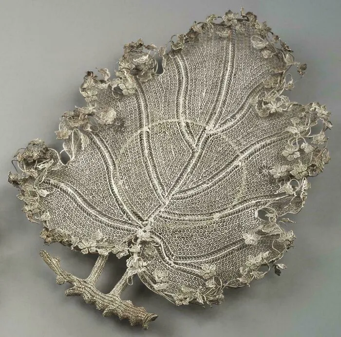 Intricate silver leaf-shaped artifact with detailed floral pattern