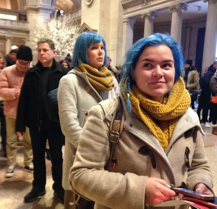 Two women with matching blue hair and mustard scarves standing in line, creating one of these strange photos.