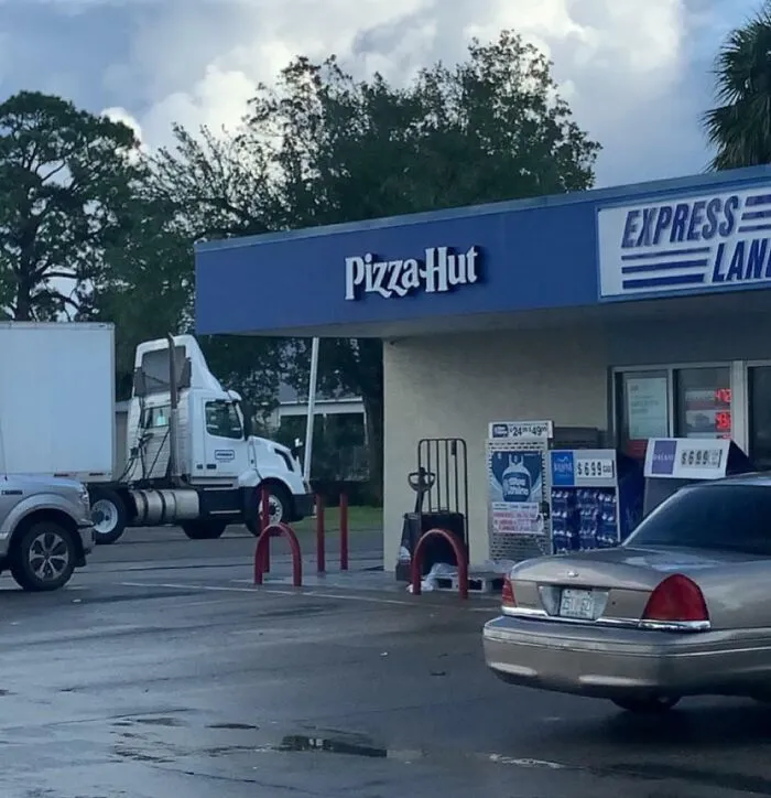 A strange photo of a blue Pizza Hut sign mounted above a gas station store.