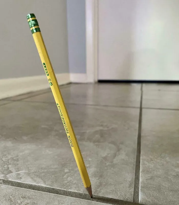 A yellow pencil standing improbably on its sharp tip in a strange photo like a glitch in reality.