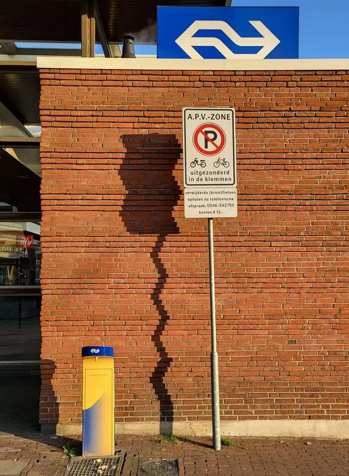 A strange photo of a distorted shadow cast by a sign post onto a brick wall.
