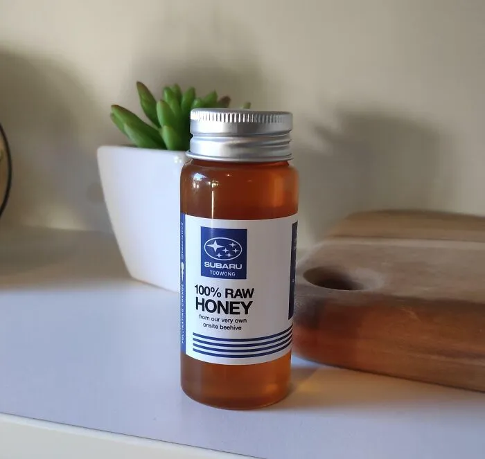 A small glass bottle of Subaru honey sitting on a shelf among strange photos.