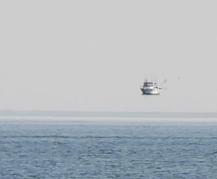 A boat appearing to float above the horizon line over the sea, seen in strange photos of optical illusions