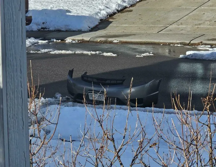 A detached car bumper sitting on a snowy street, captured in strange photos of odd real life moments