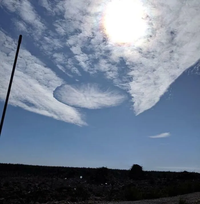 A fallstreak hole in the clouds with the sun shining above, featured in strange photos.