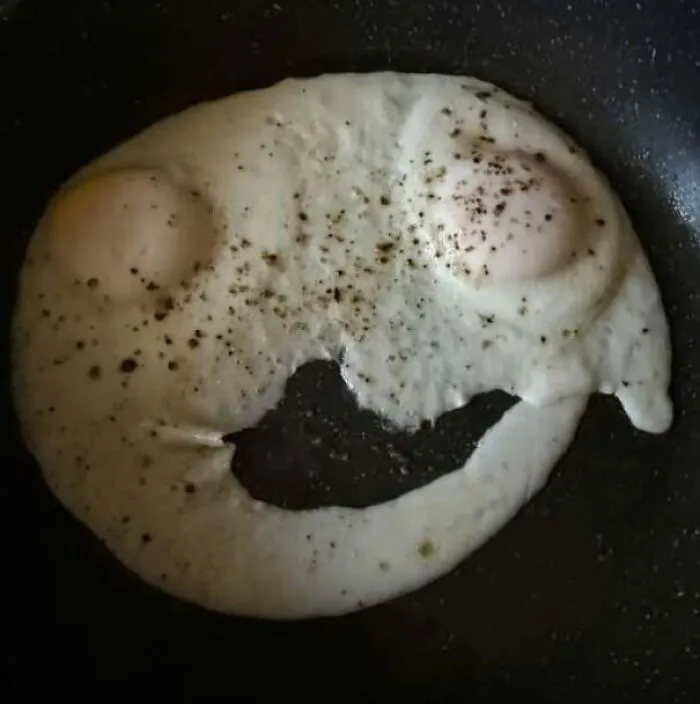 Two fried eggs on pan with pepper creating a face with eyes and mouth